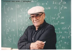 An elderly man wearing a white cap and glasses stands in front of a chalkboard filled with mathematical equations. He is holding a piece of chalk and has a thoughtful expression. Copyright information at the top left corner reads "COPYRIGHT 2005 JAIME A. ESCALANTE." This scene embodies the essence of Jaime Escalante's passion for teaching.