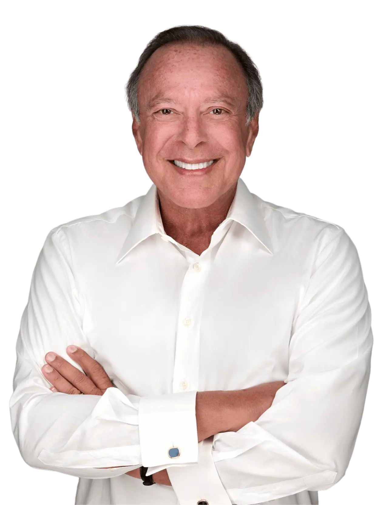 Una persona con una camisa blanca sonríe con los brazos cruzados sobre un fondo liso.