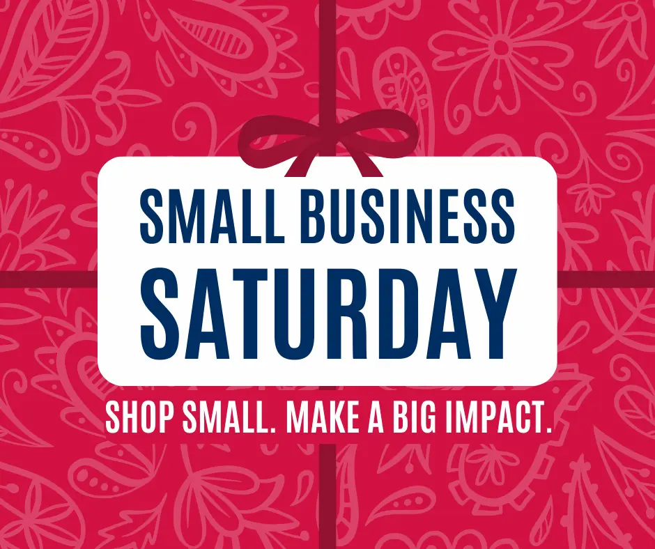 A red background with white floral patterns features a central white box with bold blue text reading "Small Business Saturday." Below in smaller text: "Shop Small. Make a Big Impact." A red bow decorates the top of the box.