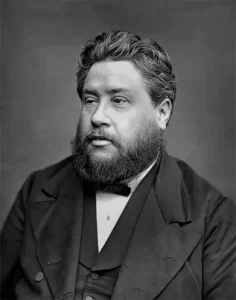 A black and white portrait of a bearded man in a formal suit and bow tie, looking to the side against a plain backdrop.