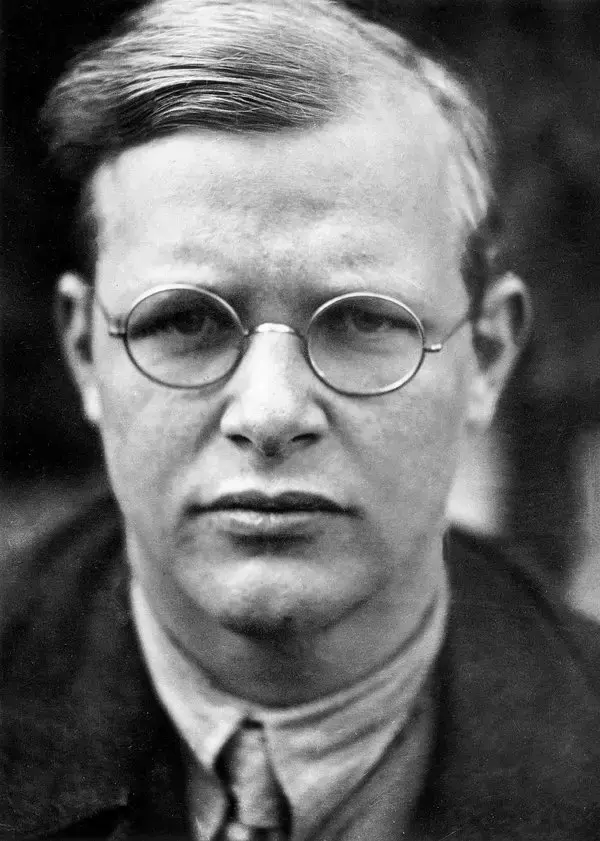 A black and white portrait of a theologian wearing round glasses and a suit. The background is blurred, emphasizing the individual's face, reminiscent of Dietrich Bonhoeffer.