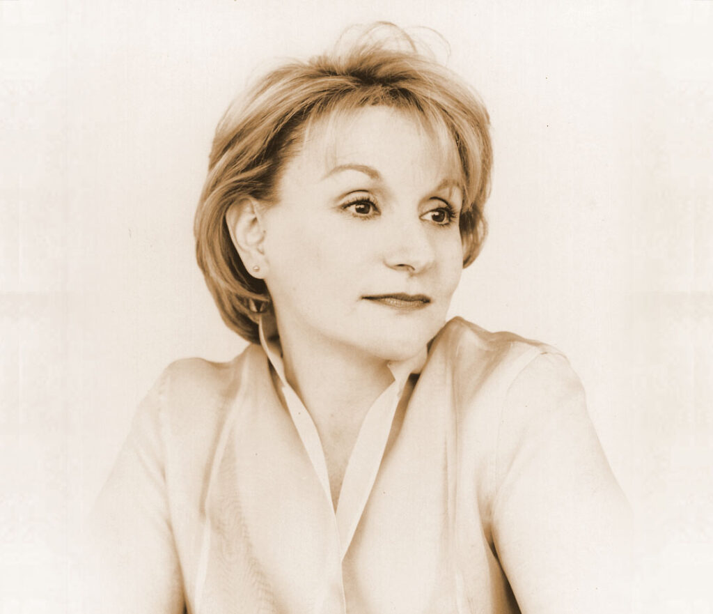 A sepia-toned portrait of a woman with short hair, wearing a light-colored blouse. She is looking slightly to the side with a calm expression.