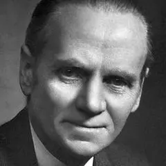 Black and white portrait of an older man wearing a suit, looking directly at the camera with a slight smile. He has neatly combed hair and a serious expression, with a dark background.