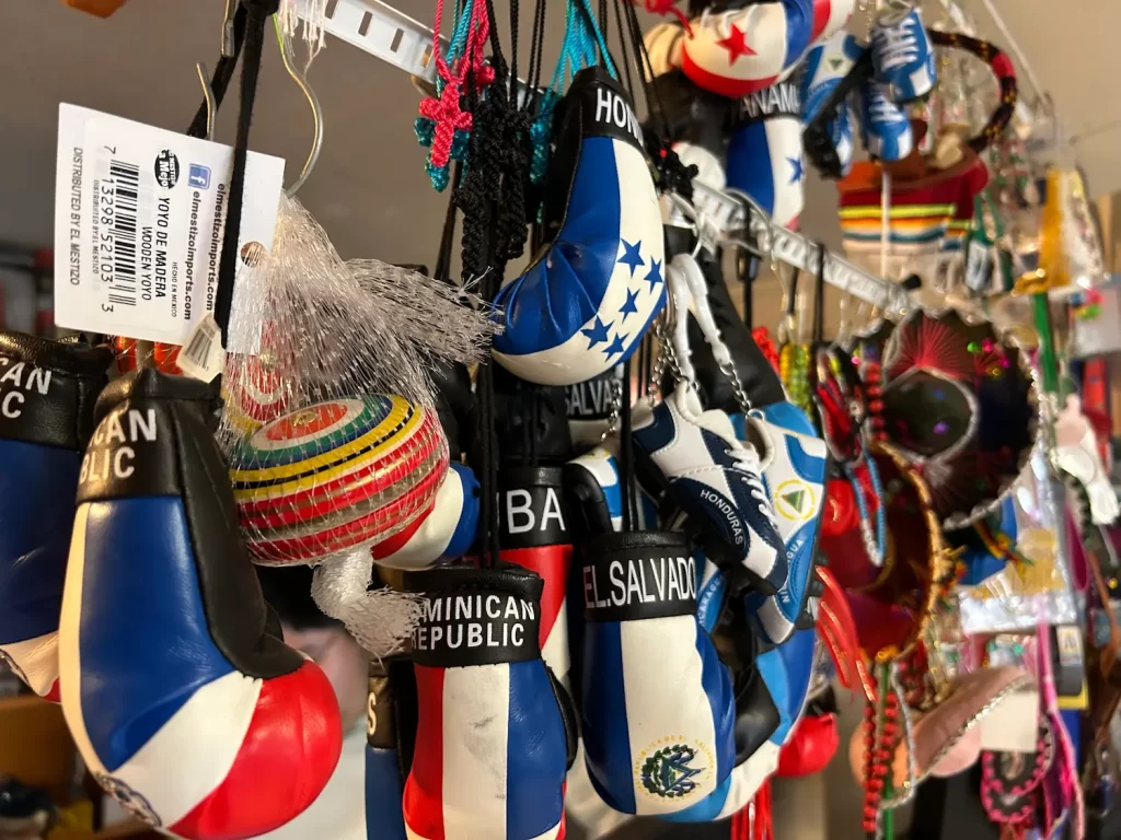 A collection of mini boxing gloves and ornaments representing various countries, like Dominican Republic and El Salvador, hanging on display. The colorful souvenirs include flags, hats, and other decorative items.