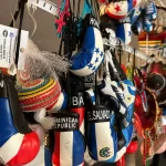 A collection of mini boxing gloves and ornaments representing various countries, like Dominican Republic and El Salvador, hanging on display. The colorful souvenirs include flags, hats, and other decorative items.