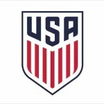 La imagen muestra el logotipo de USA Soccer, con las letras "USA" en azul marino en negrita en la parte superior de un escudo. Debajo hay rayas verticales rojas y blancas, parecidas a la bandera estadounidense, todas delineadas en azul marino.