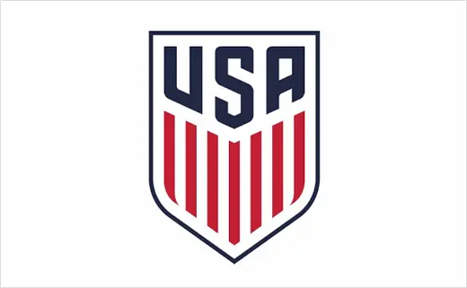 La imagen muestra el logotipo de USA Soccer, con las letras "USA" en azul marino en negrita en la parte superior de un escudo. Debajo hay rayas verticales rojas y blancas, parecidas a la bandera estadounidense, todas delineadas en azul marino.