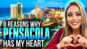 A woman in a red shirt forms a heart with her hands, expressing "8 Reasons Why Pensacola Has My Heart." Against a sunset-lit cityscape, she shares her journey on YouTube, capturing the vibrant essence of tall buildings and waterfront lights.