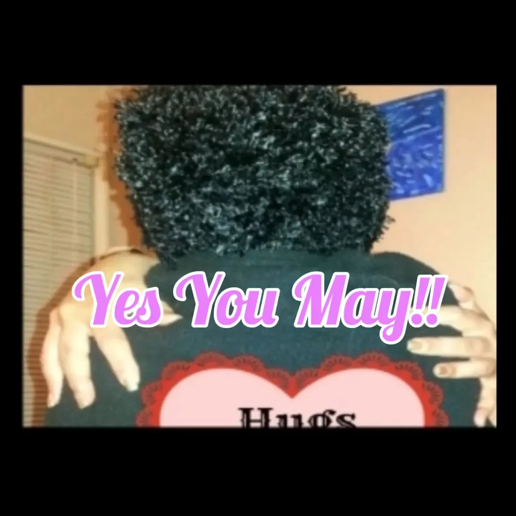 A person with curly black hair is seen from behind, hugging someone. The words "Yes You May!!" and a playful "Mother May I" vibe are written in pink and white letters. A heart shape with the word "Hugs" is partially visible.
