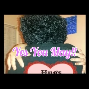 A person with curly black hair is seen from behind, hugging someone. The words "Yes You May!!" and a playful "Mother May I" vibe are written in pink and white letters. A heart shape with the word "Hugs" is partially visible.