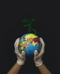 Two hands wearing white gloves gently hold a globe with a green plant sprouting from it, symbolizing environmental care and sustainability in the face of environmental cuts, against a black background.