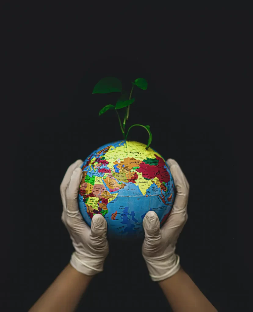 Two hands wearing white gloves gently hold a globe with a green plant sprouting from it, symbolizing environmental care and sustainability in the face of environmental cuts, against a black background.
