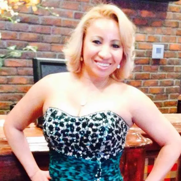 Betty Dore, Class of 2025, smiles in a strapless, sequined teal and black dress while standing indoors in front of a brick wall.