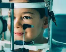 A child sits at an eye examination device, smiling slightly while undergoing a vision test at an eye clinic, highlighting the importance of pediatric eye health during childEyeAwarenessMonth.