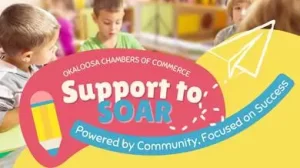Niños sentados en una mesa de clase con materiales de arte. Un colorido gráfico superpuesto dice: "Okaloosa Chambers of Commerce Support to SOAR. Powered by Community, Focused on Success", con una ilustración de un avión de papel y un lápiz.