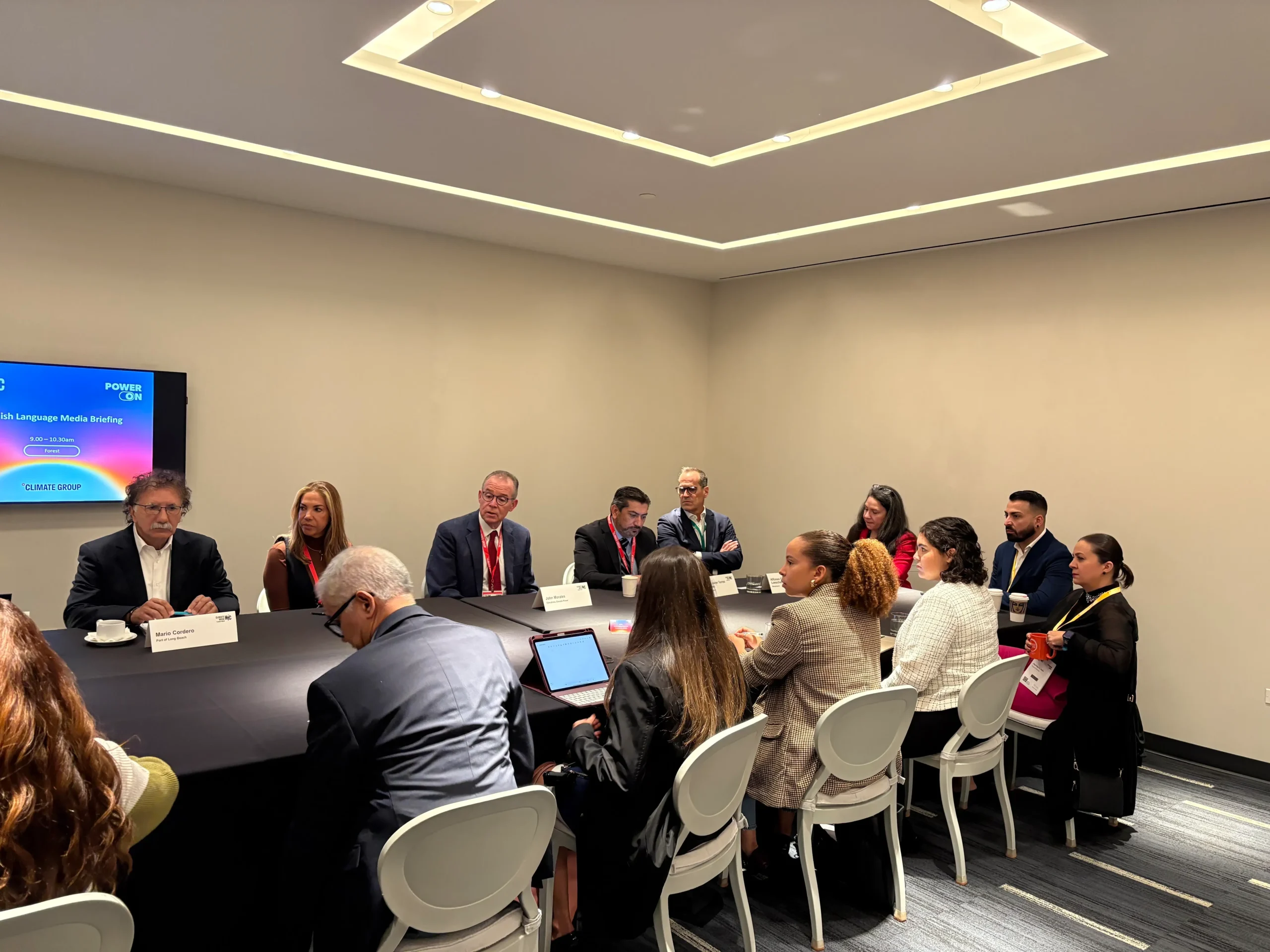 A group of professionals, including Latino Leaders, sit around a rectangular conference table in a modern meeting room in New York, engaged in discussion. A screen displays “Power of Open Language Model Building” at the front of the room.