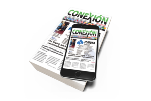 A smartphone displaying the front page of "Conexión" newspaper rests on top of a printed stack of the same newspaper, highlighting both digital and print formats in the April Digital Edition.